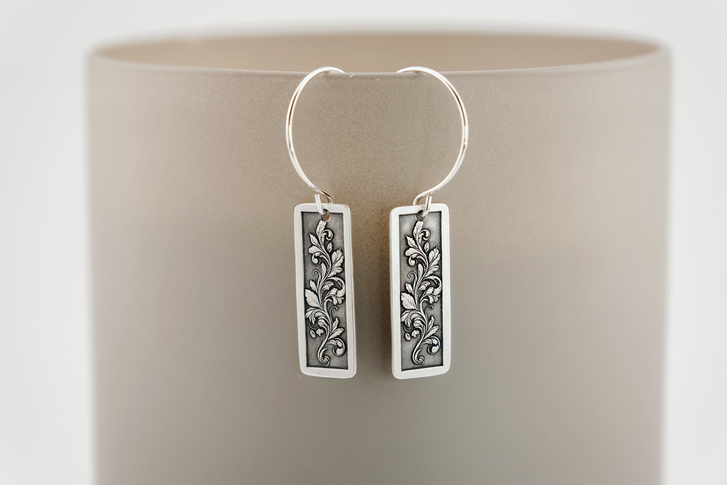 Silver earrings with engraved intricate botanical designs on a beige background