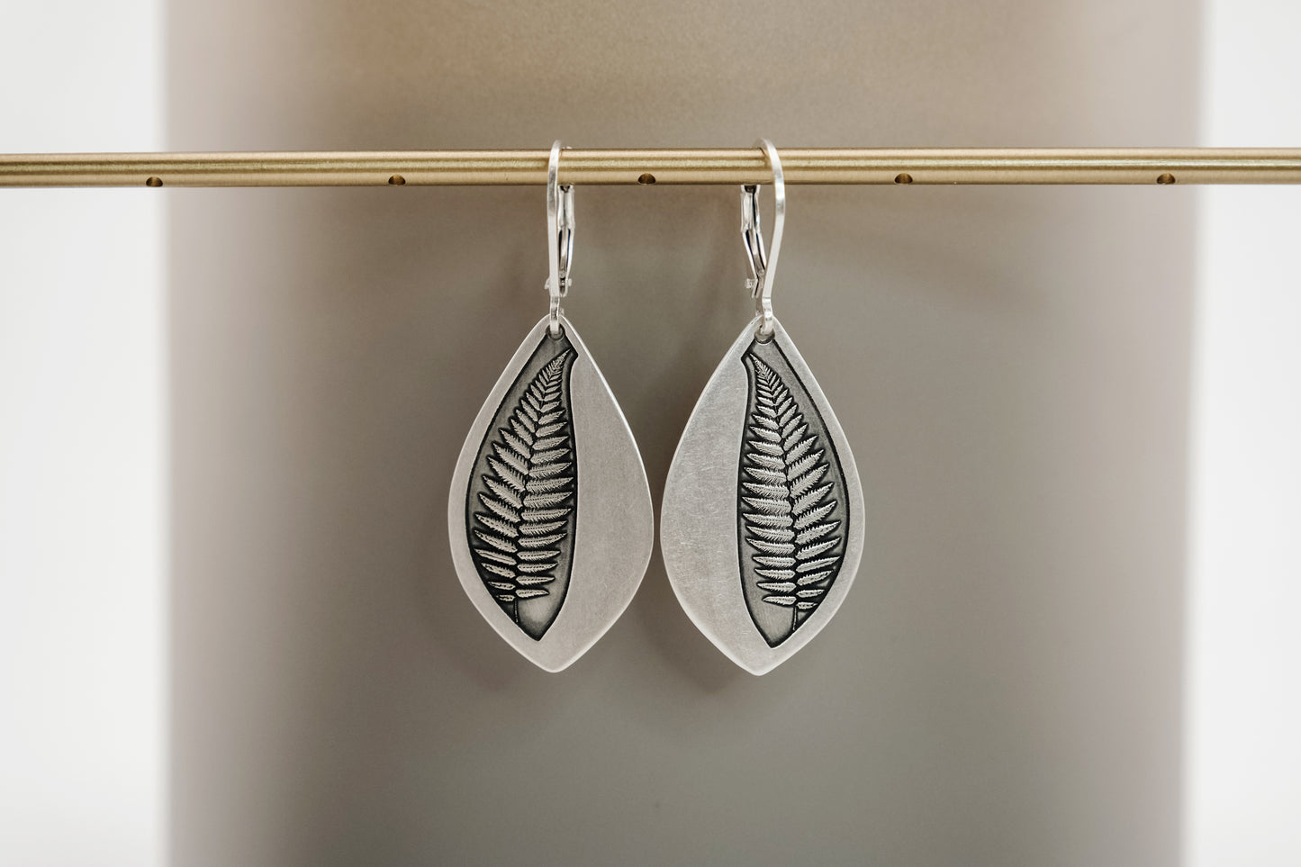 Silver leaf-shaped earrings on a beige background