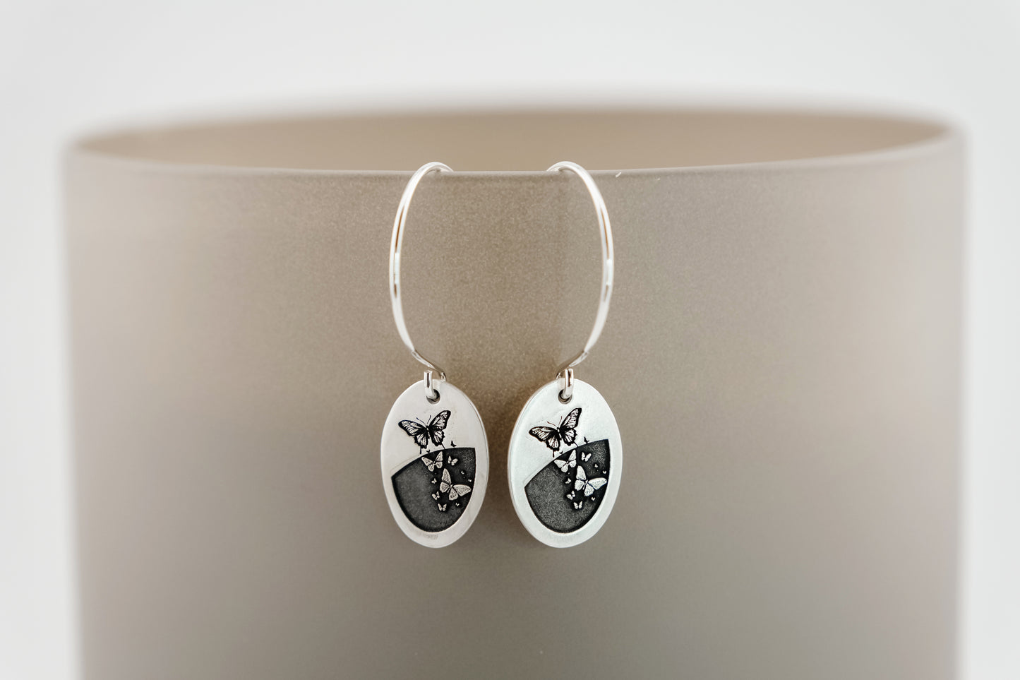 Silver earrings with butterfly designs on a beige background