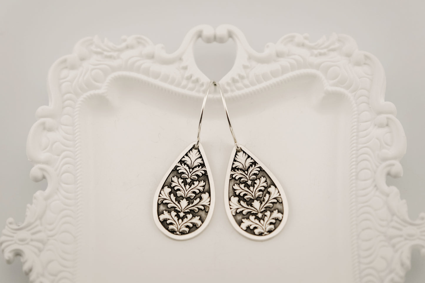 Pair of silver earrings with intricate designs on a decorative white stand.