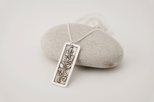 Silver pendant with an engraved floral design on a white background