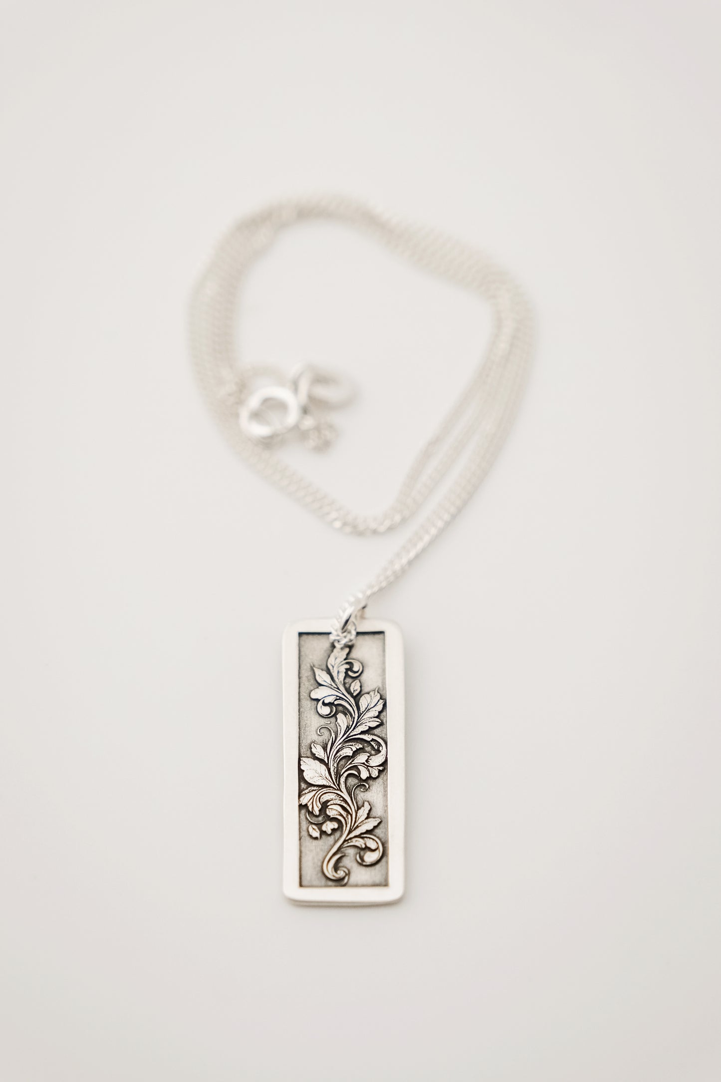Silver pendant with an engraved floral design on a white background