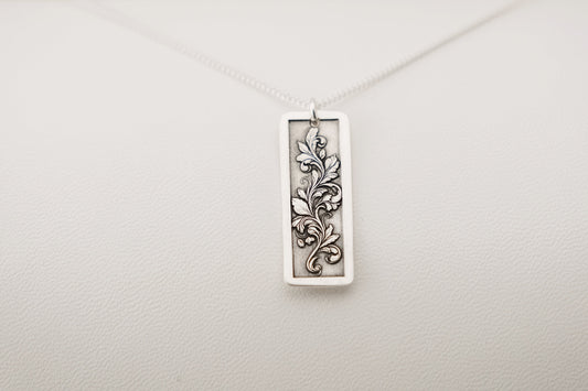 Silver pendant with an engraved floral design on a white background