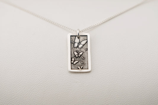 Silver necklace with a rectangular pendant engraved with butterflies laying on a white background