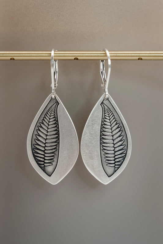 Silver leaf-shaped earrings with fern design on a gray background