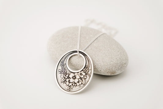 Silver necklace with floral pendant on a light gray background