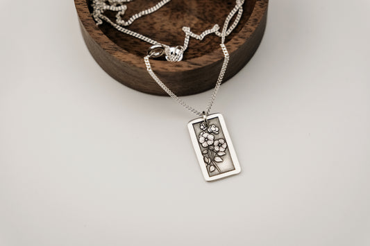 Silver necklace with a floral pendant on a wooden stand against a light background
