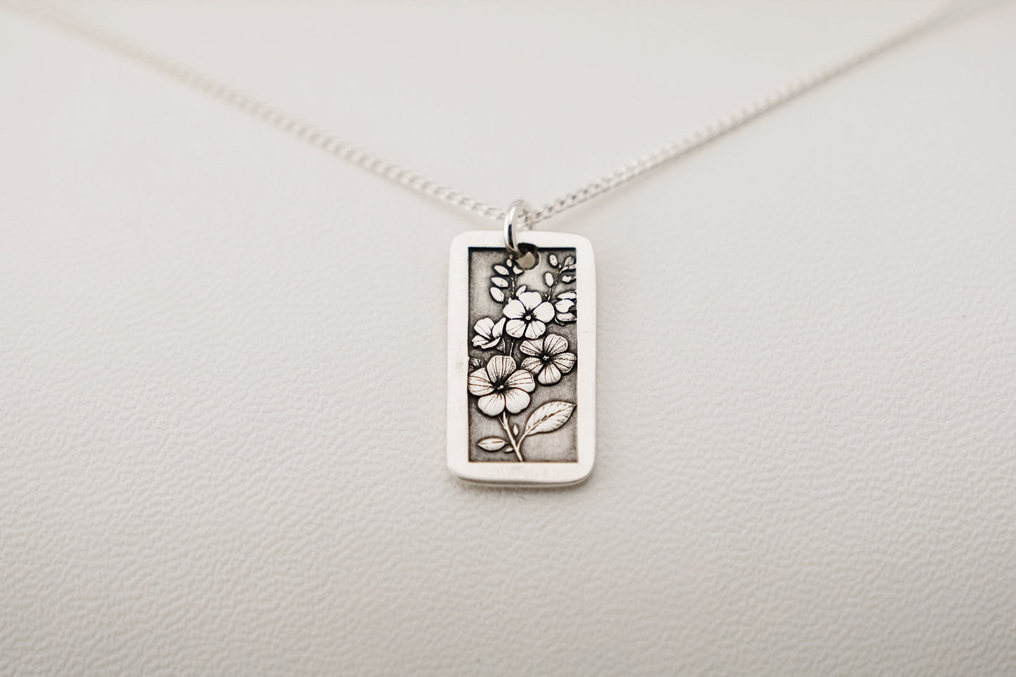 Silver necklace with a floral pendant on a light gray background