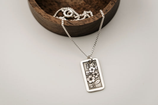 Silver necklace with a floral pendant on a wooden tray