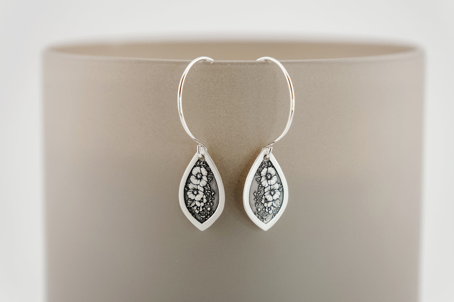 Silver teardrop earrings with floral design on a beige background