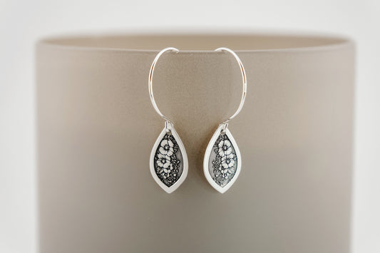 Silver teardrop earrings with floral design on a beige background