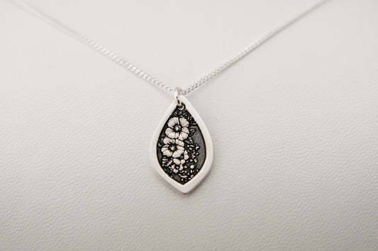 Teardrop-shaped pendant necklace featuring engraved flowers resting on a light gray background