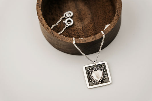 Silver necklace with a shield pendant in a wooden box on a light background