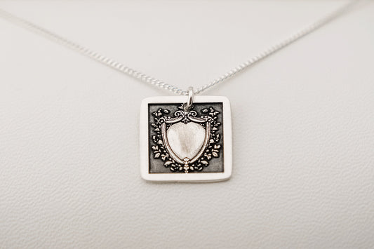 Silver necklace with a shield-shaped pendant on a light gray background