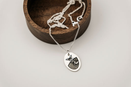 Necklace with a pendant featuring a butterfly design resting on a wooden stand against a light background