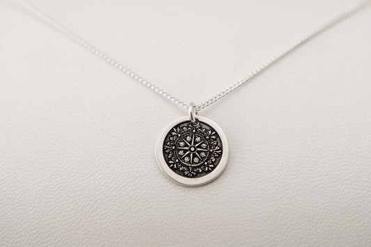 Silver necklace with a round compass pendant on a light gray background