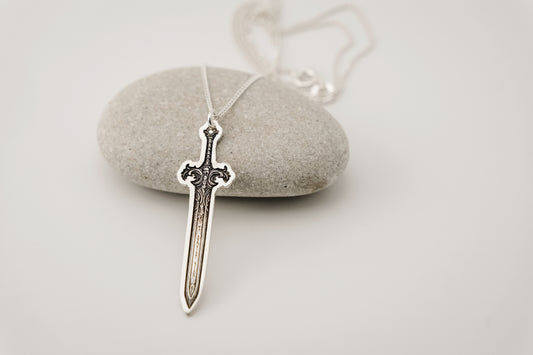 Silver sword-shaped pendant on a chain against a light gray background