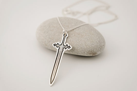 Silver sword-shaped pendant on a chain, resting on a stone surface.