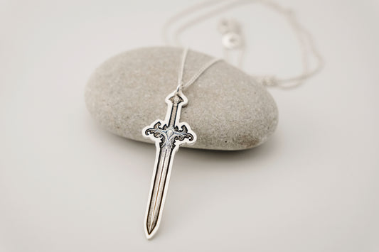 Silver sword-shaped pendant on a string, resting on a stone surface.