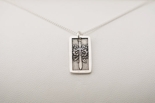Silver necklace with a rectangular pendant featuring a sword and flowers on a light gray background