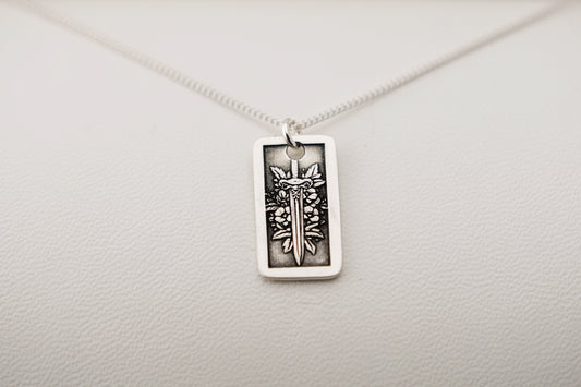 Silver necklace with a rectangular pendant featuring a sword and flowers on a light gray background