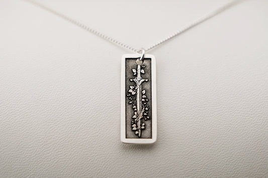 Silver pendant necklace featuring an engraved vine-wrapped sword on a light gray background