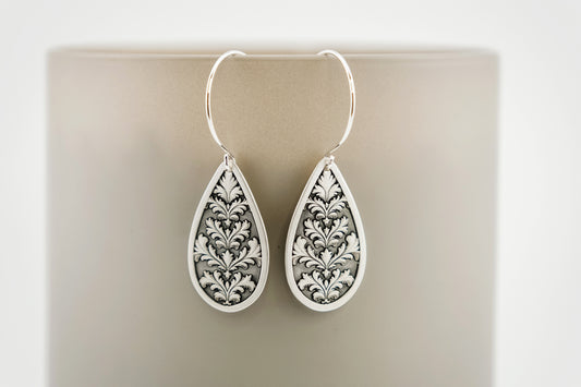 Teardrop-shaped silver earrings with intricate patterns on a beige background