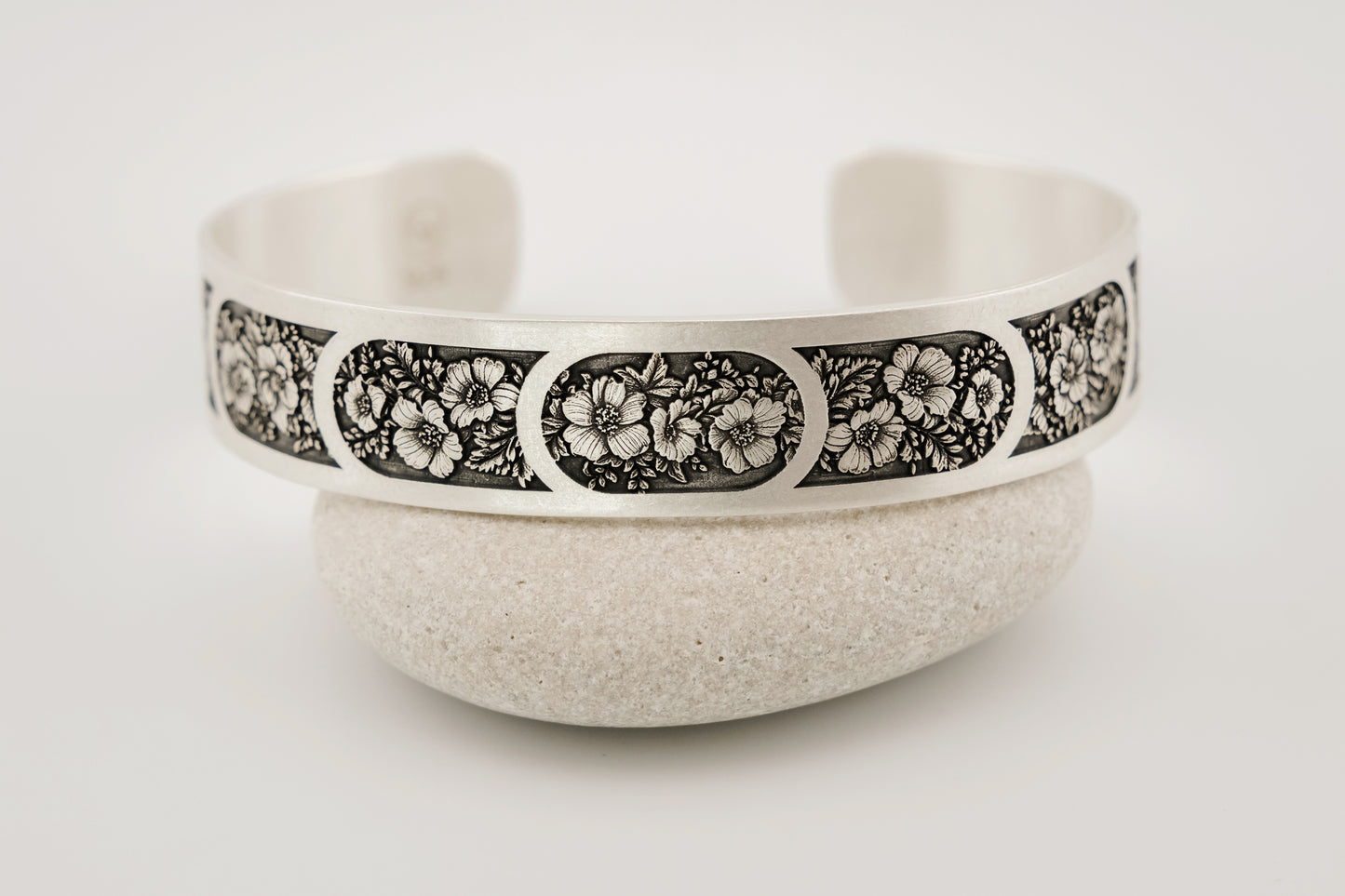 Silver bracelet with floral pattern on a white background