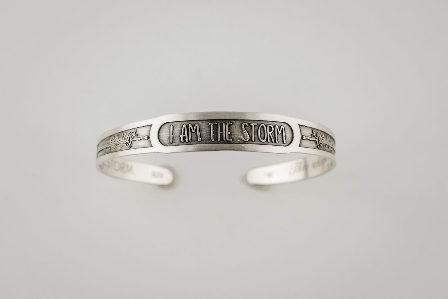 Silver bracelet with 'I AM THE STORM' engraving on a light gray background